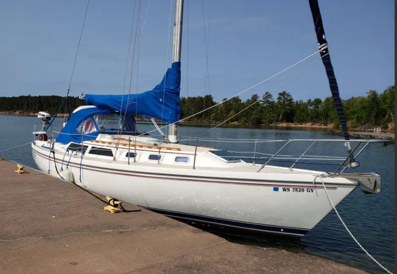 The Image of 1988 Catalina 38 MKi sailboat docked by a serene lake with blue sail cover. - 1