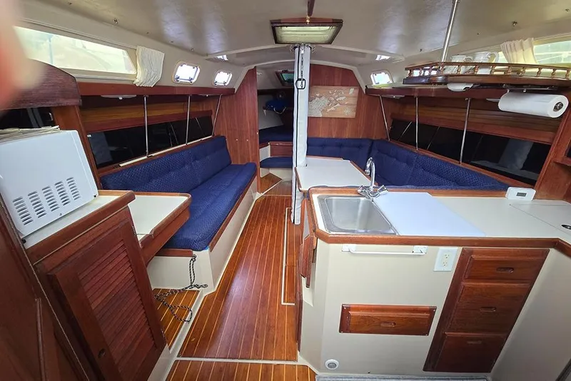 Slide: The Image of 1988 Catalina 34 mkI yacht interior with wood finish, blue seating, and compact kitchen area. - 13