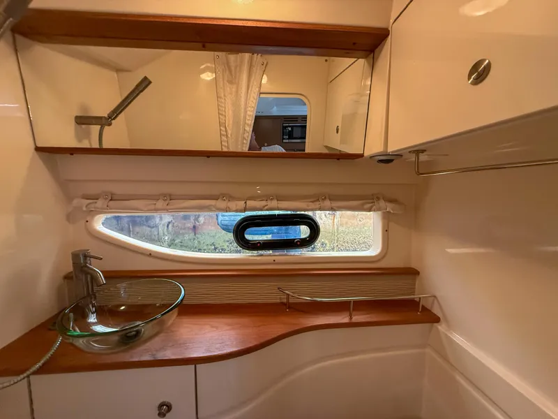 Slide: The Image of 2016 Sea Ray 350 Sundancer bathroom with glass sink, wooden accents, and porthole window. - 28