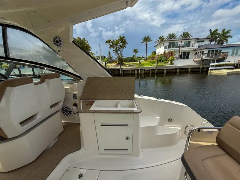 Slide: The Image of 2016 Sea Ray 350 Sundancer boat interior with seating and sink, docked near waterfront homes. - 7