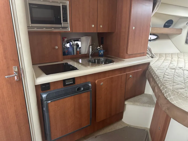 Slide: The Image of 2009 Cruisers 300 CXi Express cabin with kitchenette and bed, featuring wood cabinetry and appliances. - 7