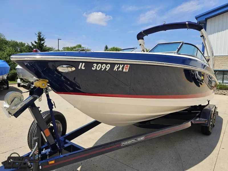 Slide: The Image of 2018 Regal 2300 Bowrider boat on trailer, parked outdoors under clear blue sky. - 16