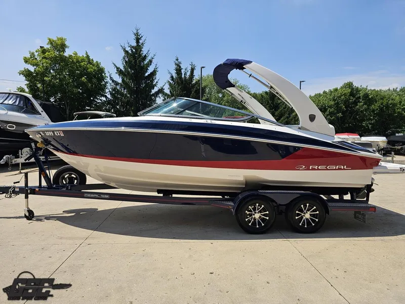 Slide: The Image of 2018 Regal 2300 Bowrider boat on trailer, parked outdoors, with trees in the background. - 19