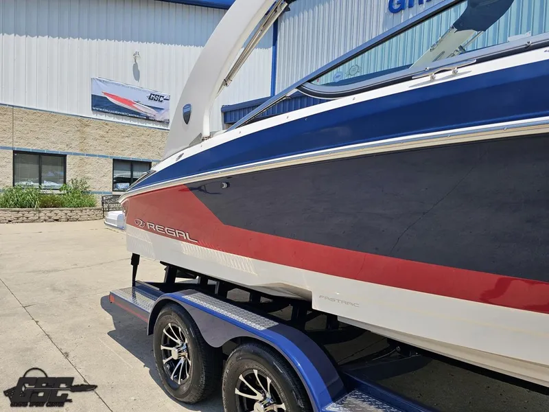 Slide: The Image of 2018 Regal 2300 Bowrider boat on trailer, blue and red design, parked outside dealership. - 4