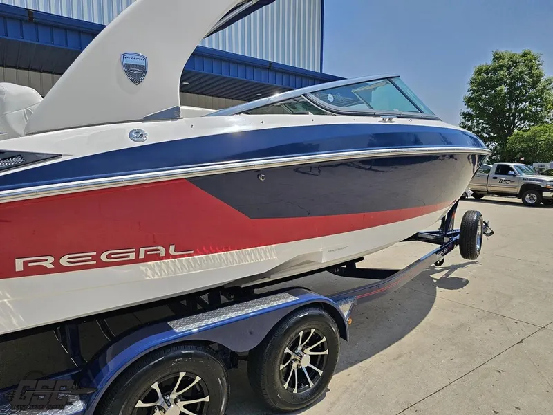 Slide: The Image of 2018 Regal 2300 Bowrider boat on trailer, blue and red design, parked outdoors. - 7