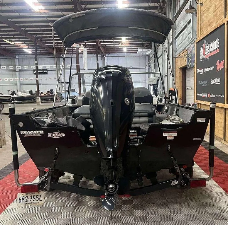 Slide: The Image of 2016 Tracker Pro Guide V-16 WT boat in a showroom, rear view with motor and canopy. - 2