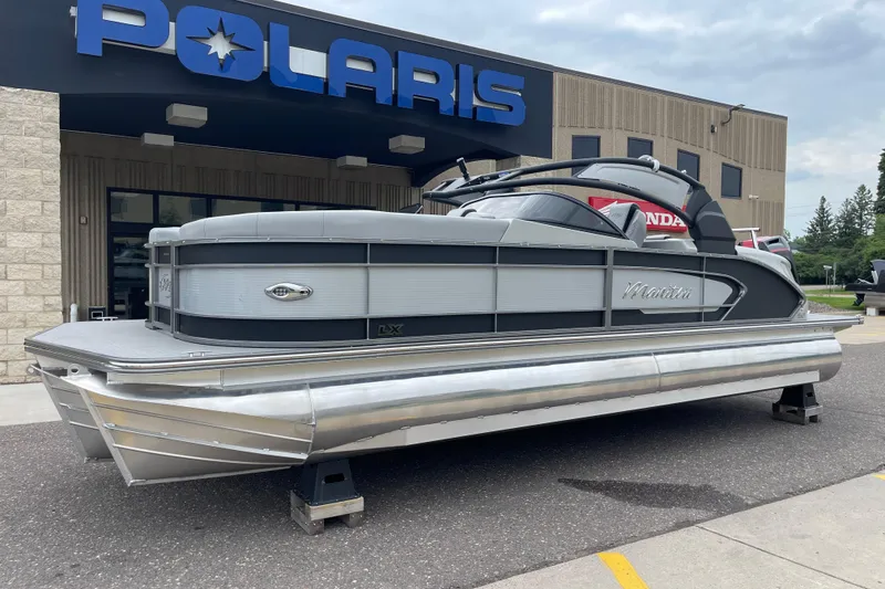 Slide: The Image of 2024 Manitou LX 25 RFXW pontoon boat displayed outside Polaris dealership. - 1