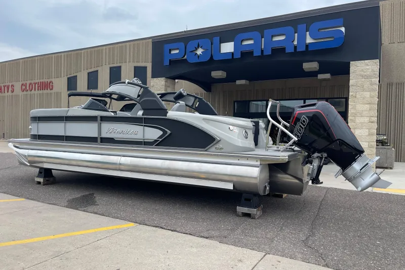 Slide: The Image of 2024 Manitou LX 25 RFXW pontoon boat displayed outside Polaris dealership. - 2