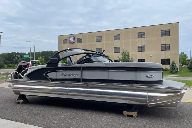 Slide: The Image of 2024 Manitou LX 25 RFXW pontoon boat displayed outdoors near a modern building. - 3