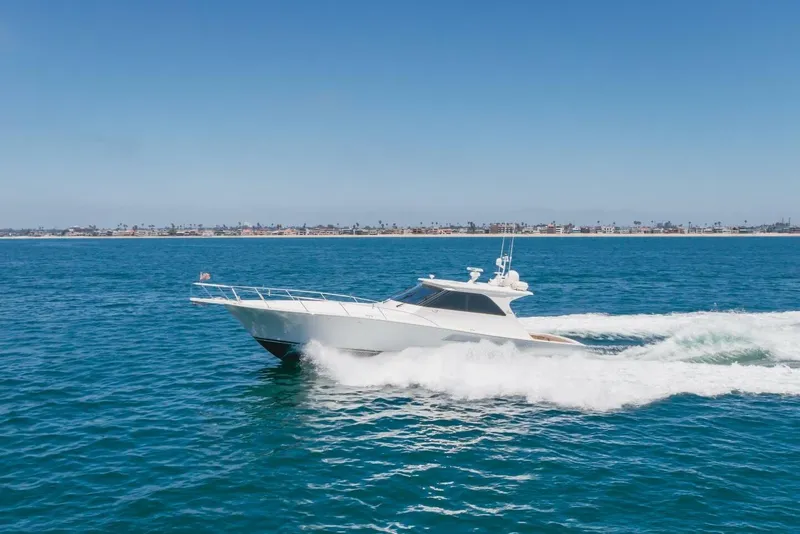 Slide: The Image of 2008 Viking 52 Sport Coupe cruising on open water, clear sky, coastal background. - 46