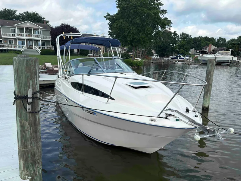 The Image of 2006 Bayliner 245 boat docked by a lakeside house, surrounded by trees and calm water. - 0