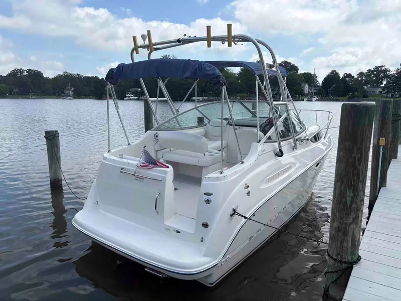 Slide: The Image of 2006 Bayliner 245 boat docked on a calm lake under a partly cloudy sky. - 2