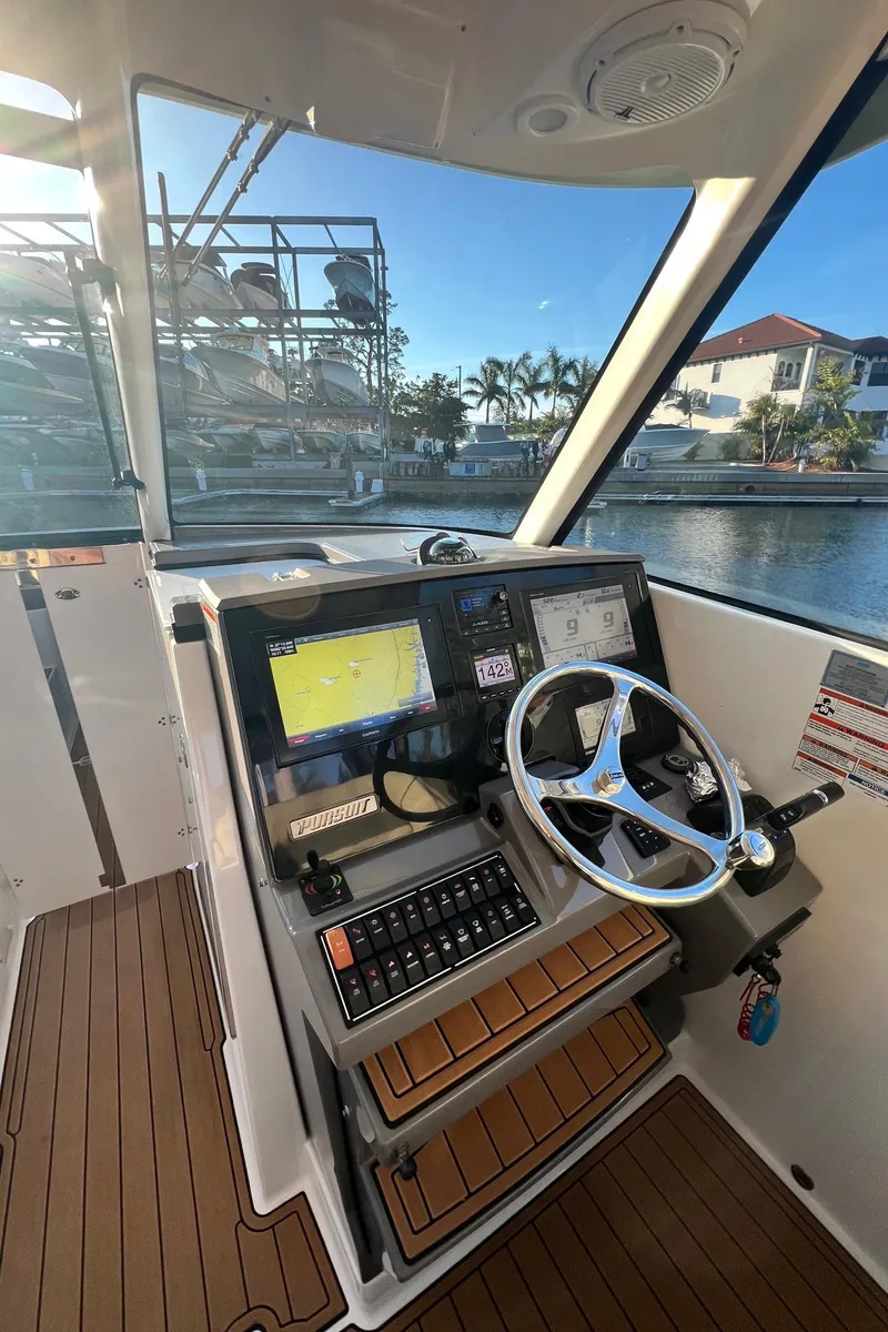 Slide: The Image of 2019 Pursuit 325 DC boat helm with navigation screens and steering wheel, dockside view. - 12