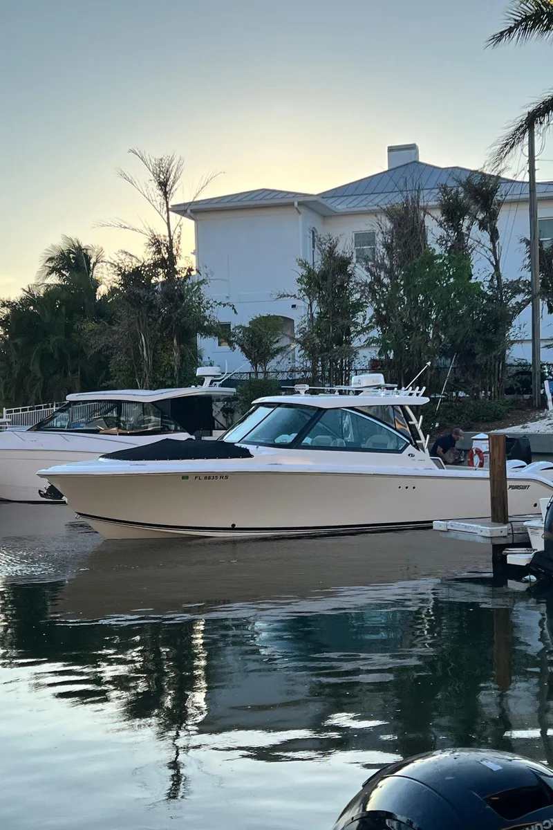 Slide: The Image of 2019 Pursuit 325 DC boat docked by waterfront home, surrounded by palm trees. - 2