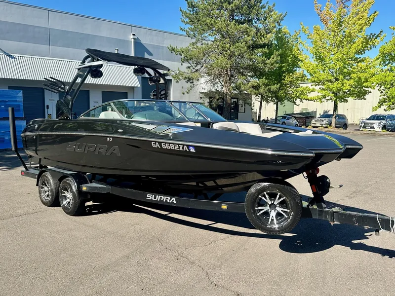 Slide: The Image of 2013 Supra SA350 boat on trailer, parked outdoors, with trees and building in background. - 5