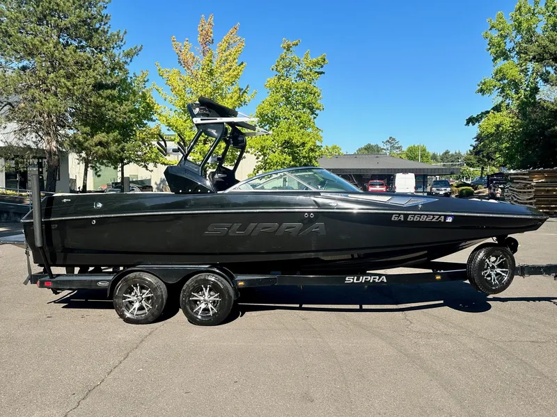 Slide: The Image of 2013 Supra SA350 boat on trailer, parked outdoors, surrounded by trees and buildings. - 6