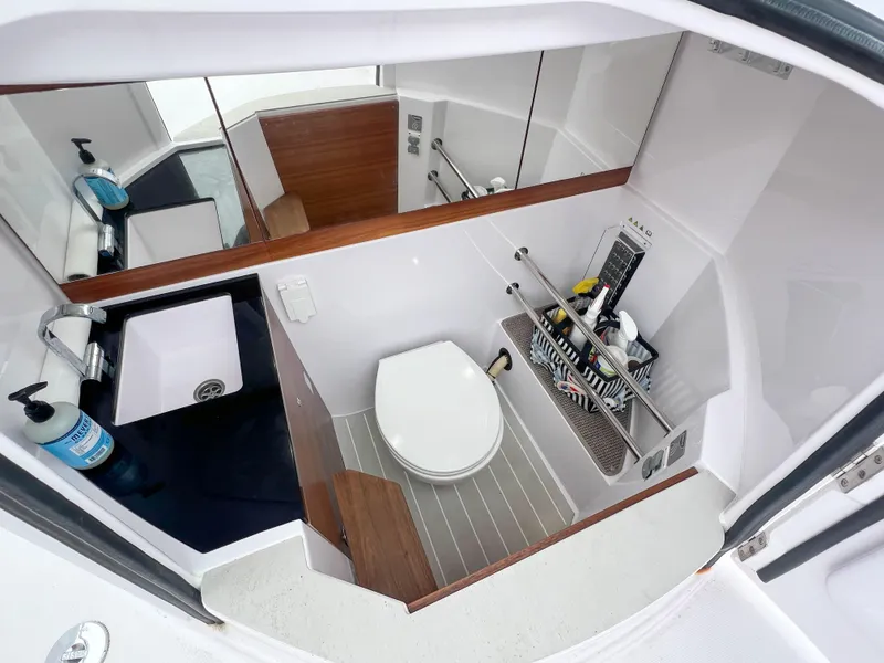 Slide: The Image of 2022 Axopar 28 Cabin Aft Cabin bathroom with toilet, sink, and storage shelves. - 26