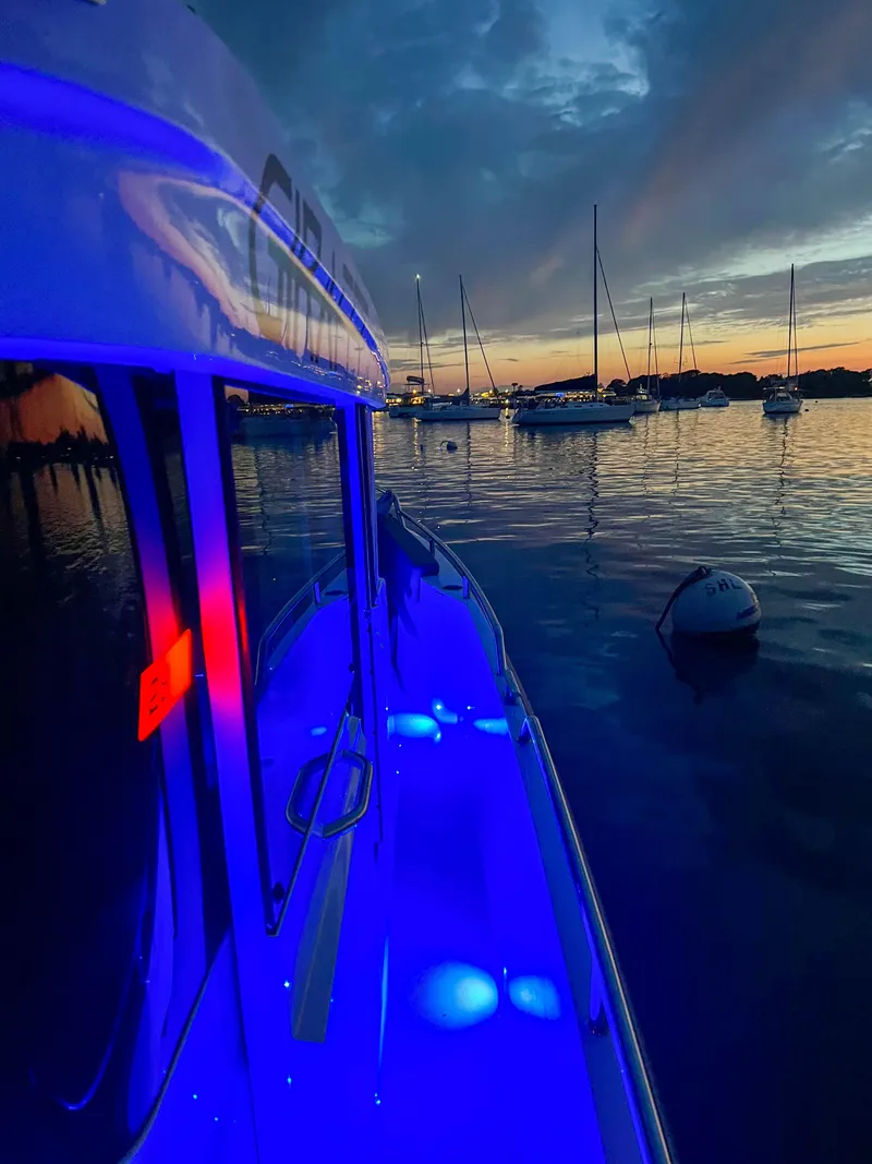 Slide: The Image of 2022 Axopar 28 Cabin Aft illuminated at sunset, docked with sailboats in the background. - 30