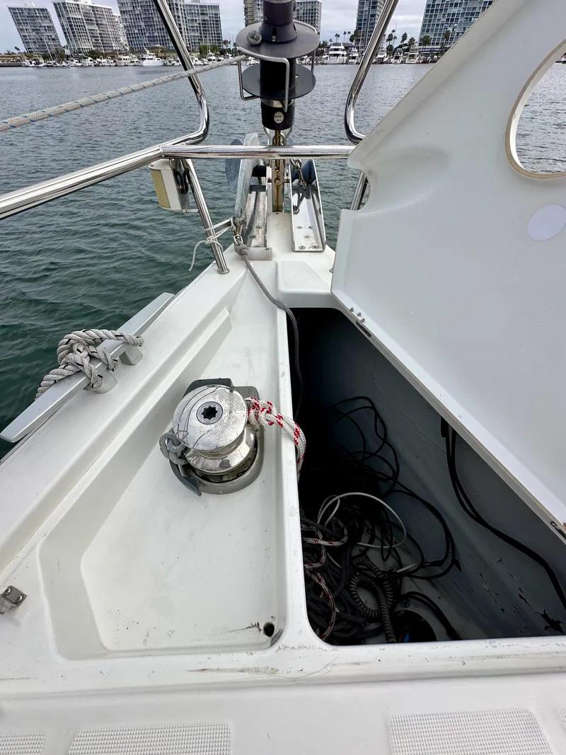 Slide: The Image of Beneteau Sense 43 sailboat deck with open storage compartment, winch, and marina view. - 23