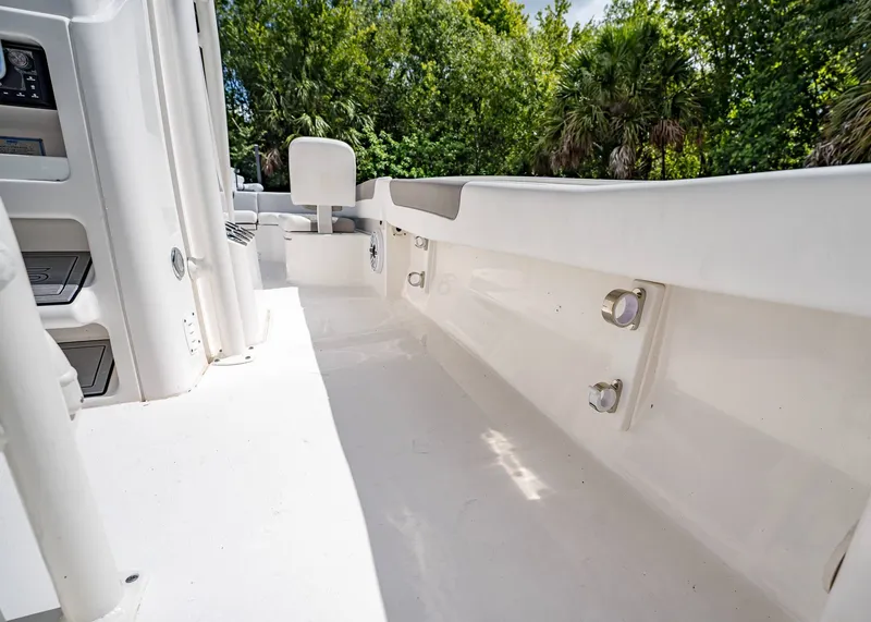 Slide: The Image of 2024 Caymas 26 HB boat interior with sleek white deck and seating, surrounded by lush greenery. - 16