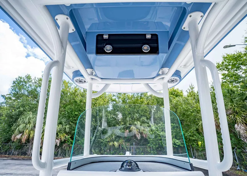 Slide: The Image of 2024 Caymas 26 HB boat console with blue T-top and speakers, surrounded by trees. - 25