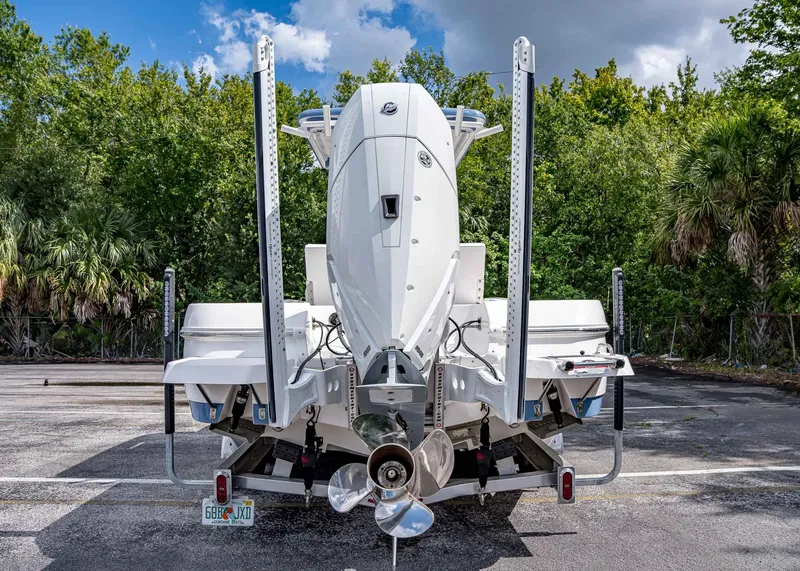 Slide: The Image of 2024 Caymas 26 HB boat rear view, parked with lush greenery background. - 9