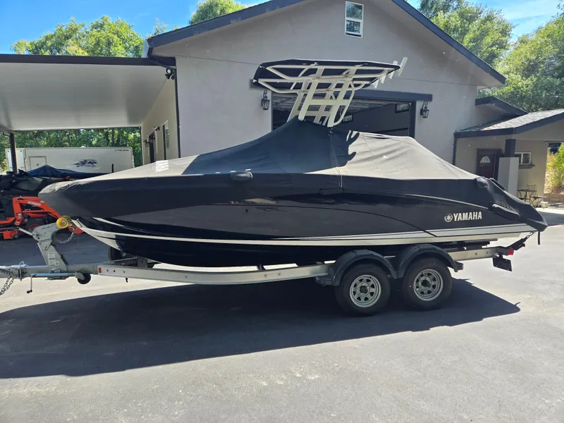 Slide: The Image of 2022 Yamaha Boats 210 FSH Deluxe covered on trailer, parked in driveway. - 4