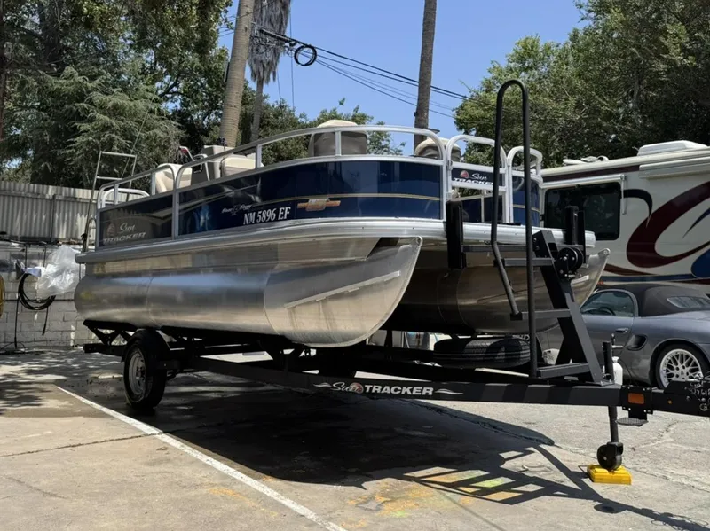 Slide: The Image of 2023 Sun Tracker Bass Buggy 16 XL Select pontoon boat on trailer, parked outdoors. - 2