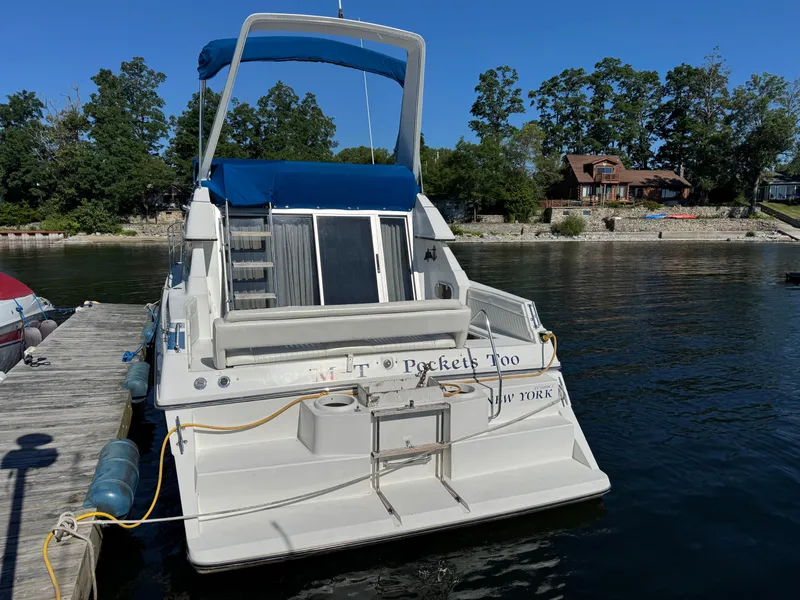 Slide: The Image of 1990 Carver 30 Santego boat docked by a lakeside with trees and house in background. - 2