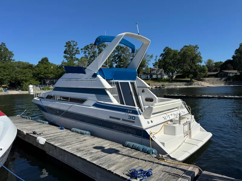 The Image of 1990 Carver 30 Santego boat docked on a sunny day, surrounded by trees and water. - 1