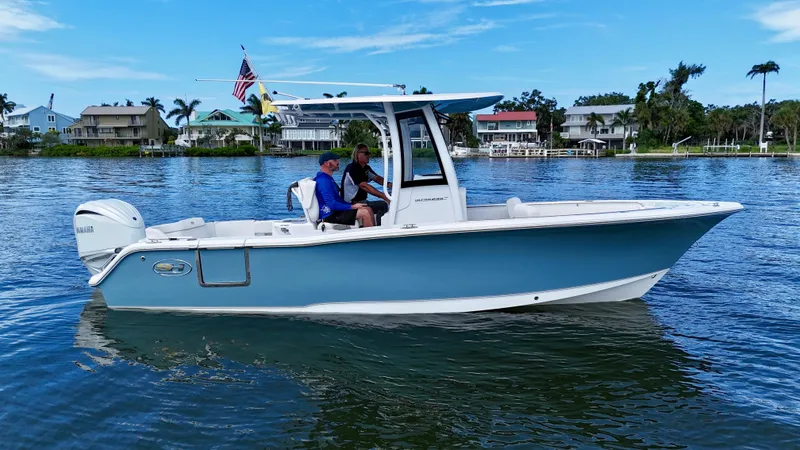 Slide: The Image of 2024 Sea Hunt Ultra 239 SE boat on calm water, with houses and palm trees in the background. - 10