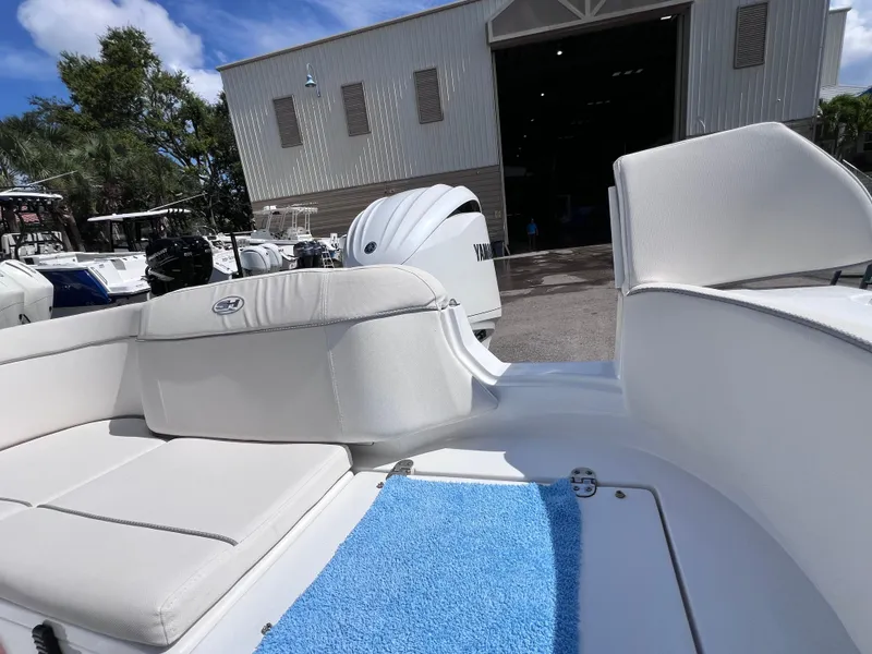 Slide: The Image of 2024 Sea Hunt Ultra 239 SE boat interior with white seating and blue mat, parked near a warehouse. - 29
