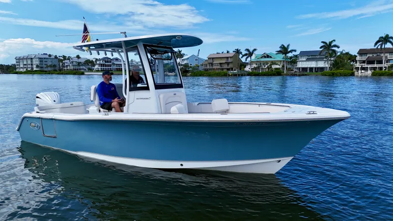 Slide: The Image of 2024 Sea Hunt Ultra 239 SE boat on calm water, with houses and palm trees in the background. - 9