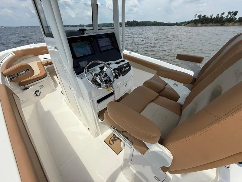 Slide: The Image of 2023 NauticStar 28 XS boat interior with tan seating and modern dashboard on a lake. - 17
