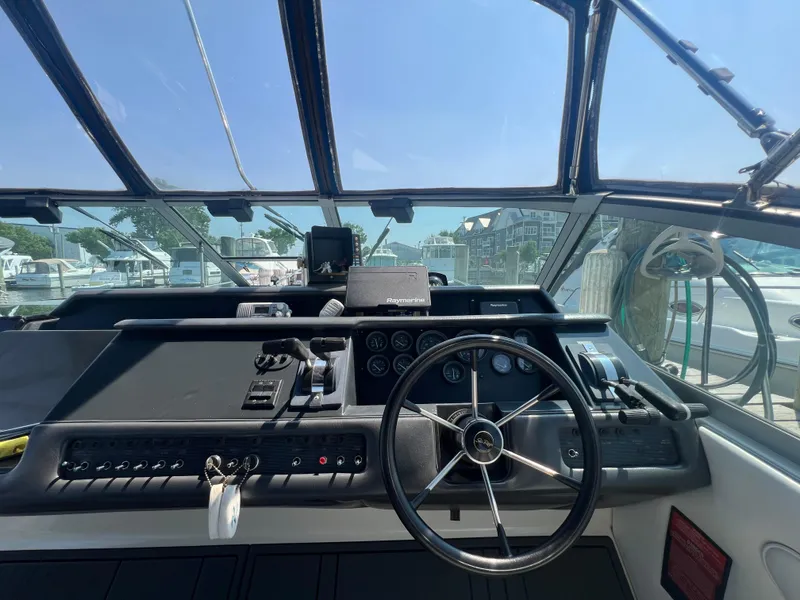 Slide: The Image of 1991 Sea Ray 310 Sundancer helm with steering wheel and control panel, docked at marina. - 13