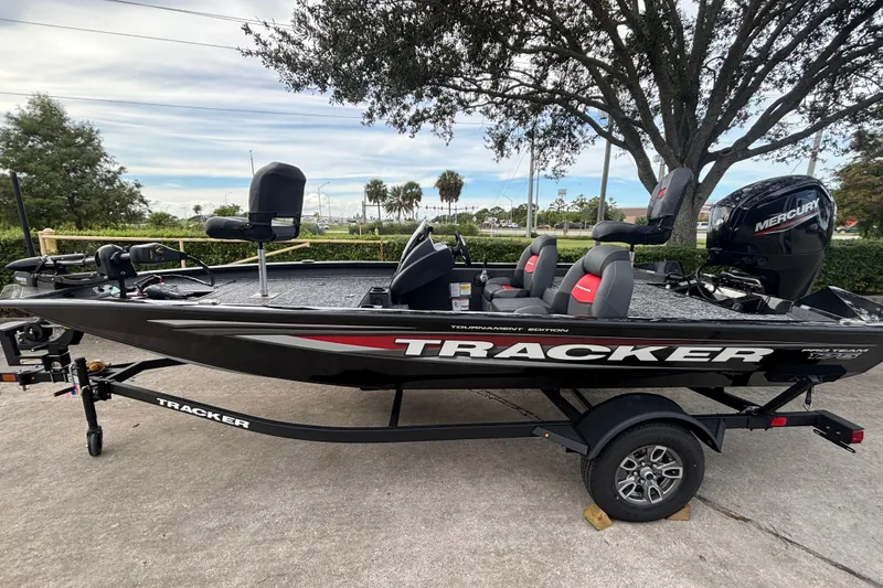 The Image of 2025 Tracker Pro Team 175 boat on trailer, parked outdoors under trees. - 0