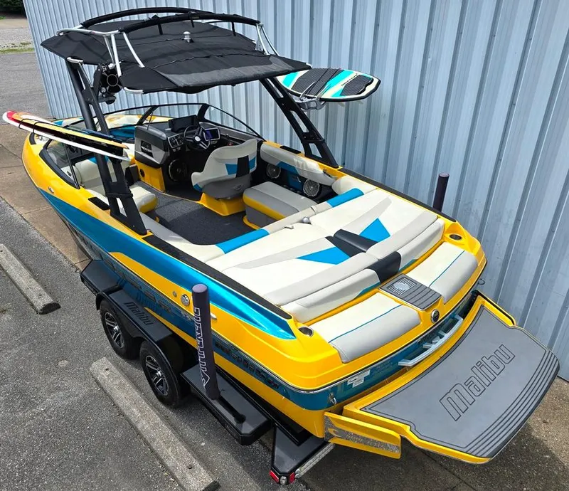 Slide: The Image of 2015 Malibu Wakesetter 22 VLX Surf Gate boat with vibrant yellow and blue design on trailer. - 2