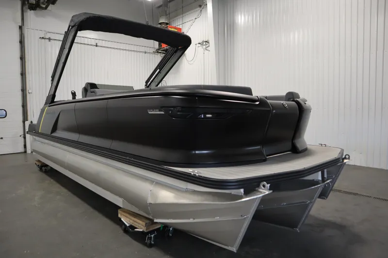 Slide: The Image of 2025 Manitou 24 Explore Switchback Trifold Tritoon in a showroom, sleek black design. - 3