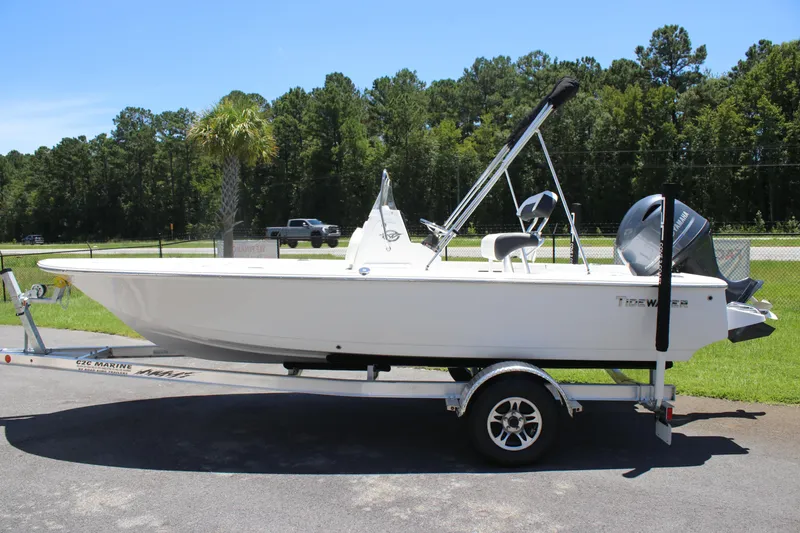 Slide: The Image of 2026 Tidewater 1910 Bay Max boat on trailer, parked outdoors with trees in background. - 2