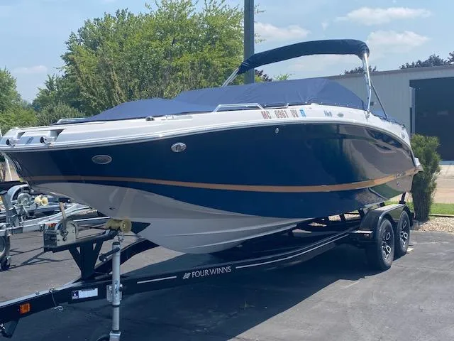 Slide: The Image of 2023 Four Winns HD3 boat on trailer, blue and white design, parked outdoors. - 2