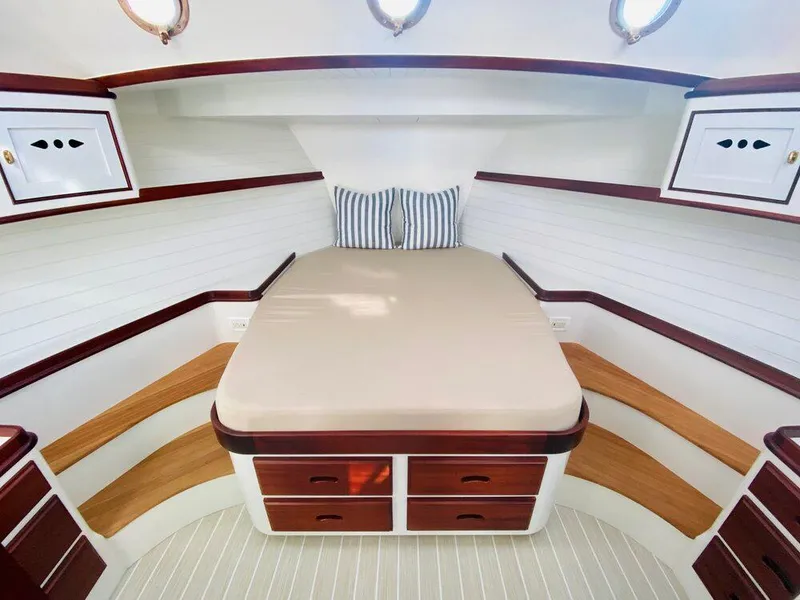 Slide: The Image of 2021 Mussel Ridge downeast boat cabin with bed, wooden accents, and striped pillows. - 12