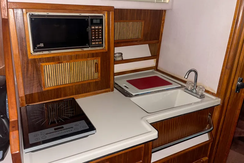 Slide: The Image of 1987 Sea Ray 300 Sundancer galley with microwave, stove, sink, and wooden cabinetry. - 27