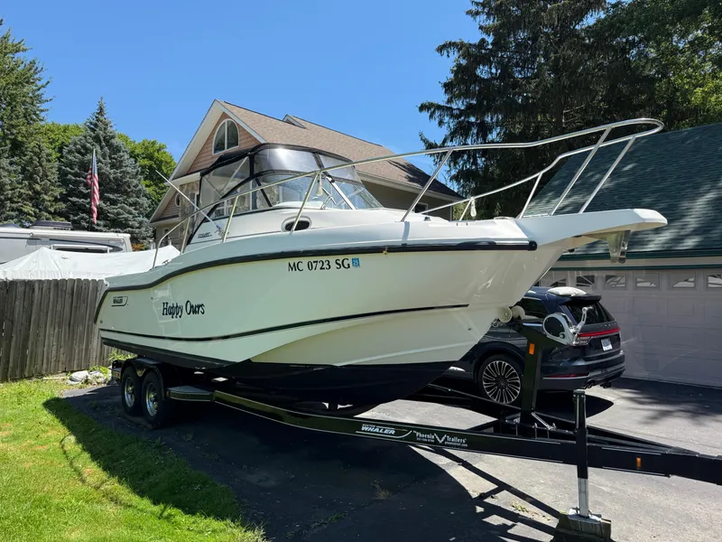 Slide: The Image of 2002 Boston Whaler 255 Conquest boat on trailer in driveway, surrounded by trees and house. - 3