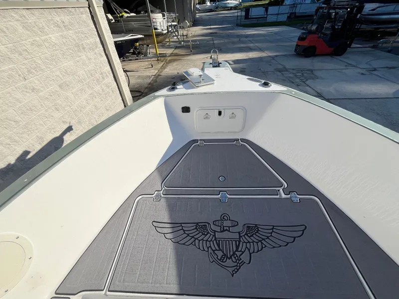 Slide: The Image of 2003 Pro-Line 25 Sport CC boat deck with anchor emblem, docked near a forklift. - 23