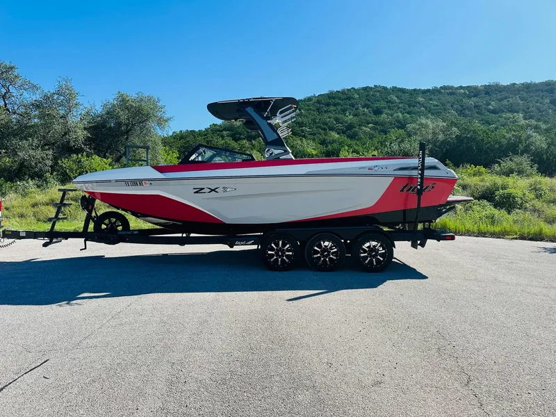 Slide: The Image of 2020 Tigé 25ZX boat on trailer, red and white, parked on road with scenic background. - 11