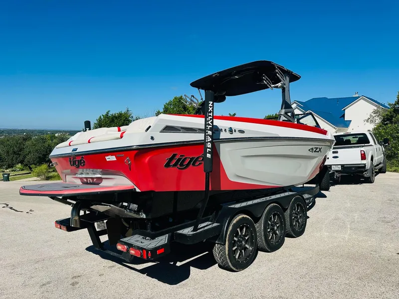 Slide: The Image of 2020 Tigé 25ZX boat on trailer, red and white design, parked outdoors. - 7