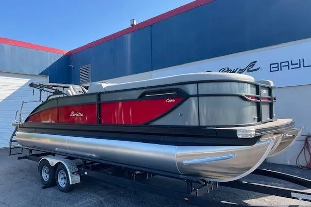 The Image of 2026 Barletta C24UC pontoon boat on trailer, featuring sleek red and gray design. - 0