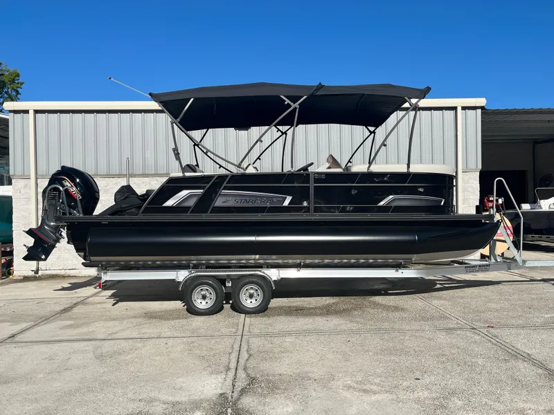 The Image of 2025 Starcraft EXS-3 pontoon boat on trailer, parked outdoors under clear blue sky. - 0