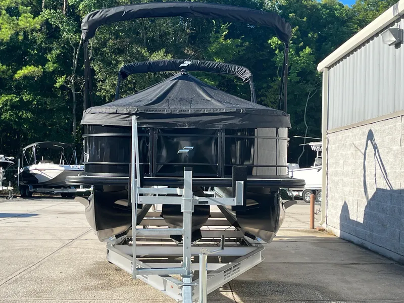 Slide: The Image of 2025 Starcraft EXS-3 pontoon boat on trailer, parked outdoors near trees and building. - 4