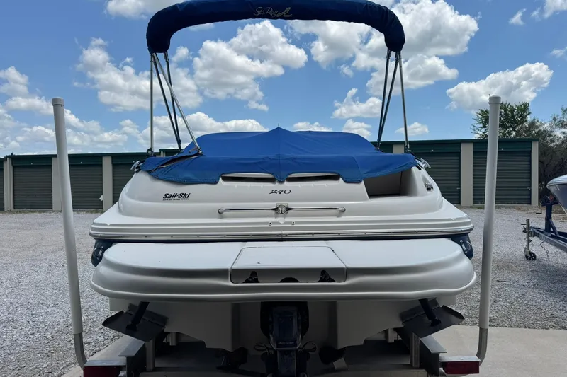 Slide: The Image of 2002 Sea Ray 240 Sundeck boat with blue cover, parked outdoors under a cloudy sky. - 2